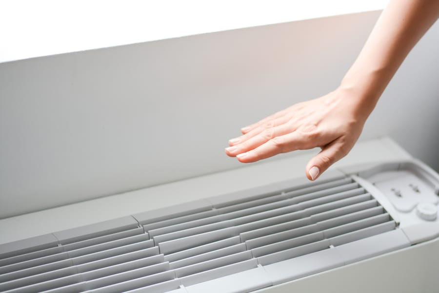 A hand testing an AC unit to see if an emergency repaired is required.